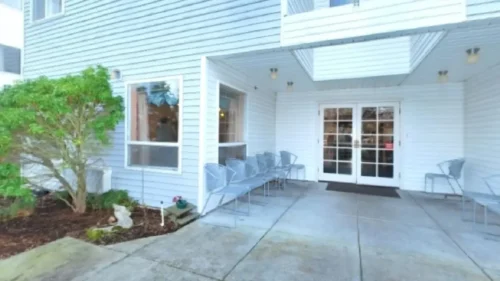A covered outdoor patio with blue siding, double doors, and several blue metal chairs