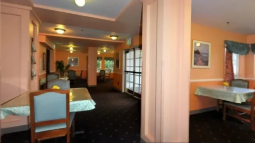 A dining room with orange walls, a dark patterned carpet, and several tables with patterned tablecloths and chairs