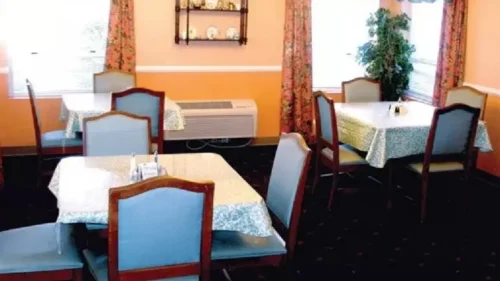 A dining room with orange walls, floral curtains, tables with patterned tablecloths, and light blue chairs
