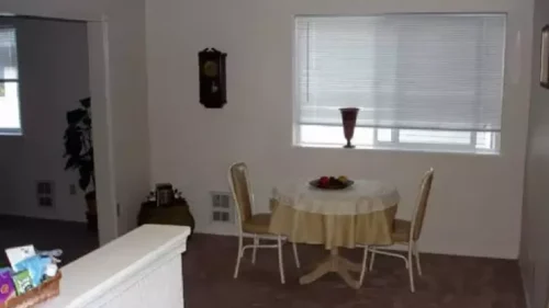 A small dining area in an apartment with a round table, two chairs, and a window with blinds